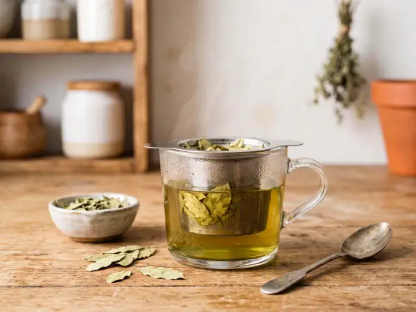 Infusion de feuille de séné, danger potentiel pour la santé. Une tasse de thé fumant avec des feuilles dans un infuseur, à côté d'un bol de feuilles séchées et d'une cuillère.